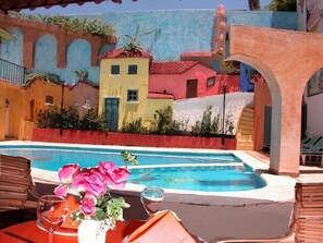 A pool area with a table set for dining, surrounded by colorful buildings. - Zihuatanejo Centro (Zihuatanejo)