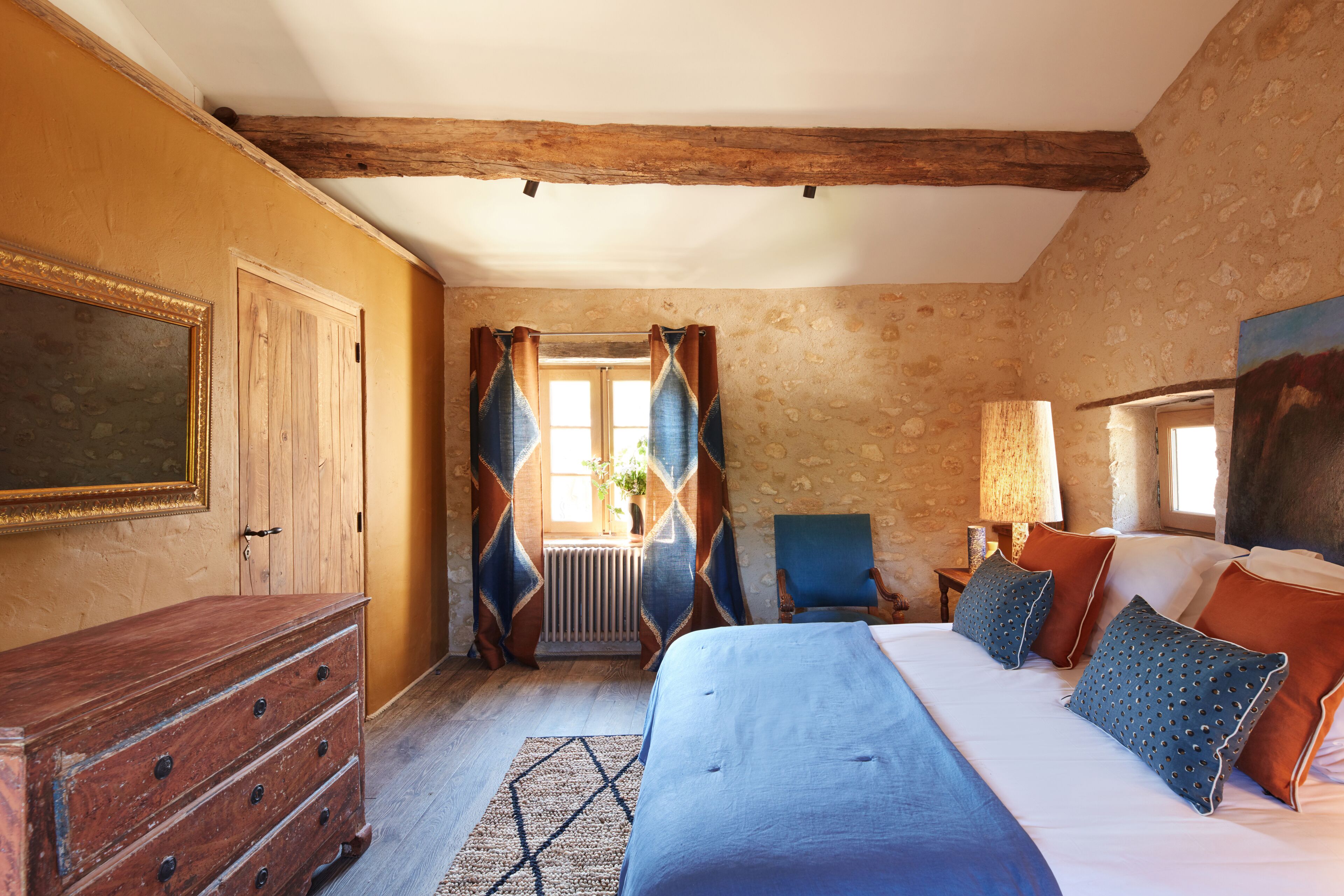 Ein Schlafzimmer mit einem Holzkasten, einem Bett mit blauer Bettwäsche und einem Sessel.