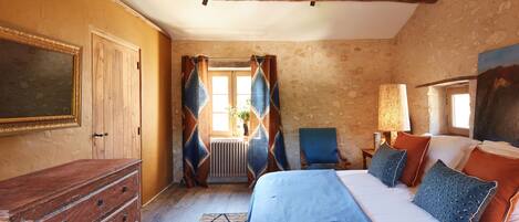 A bedroom with a wooden dresser, a bed with blue bedding, and a chair.