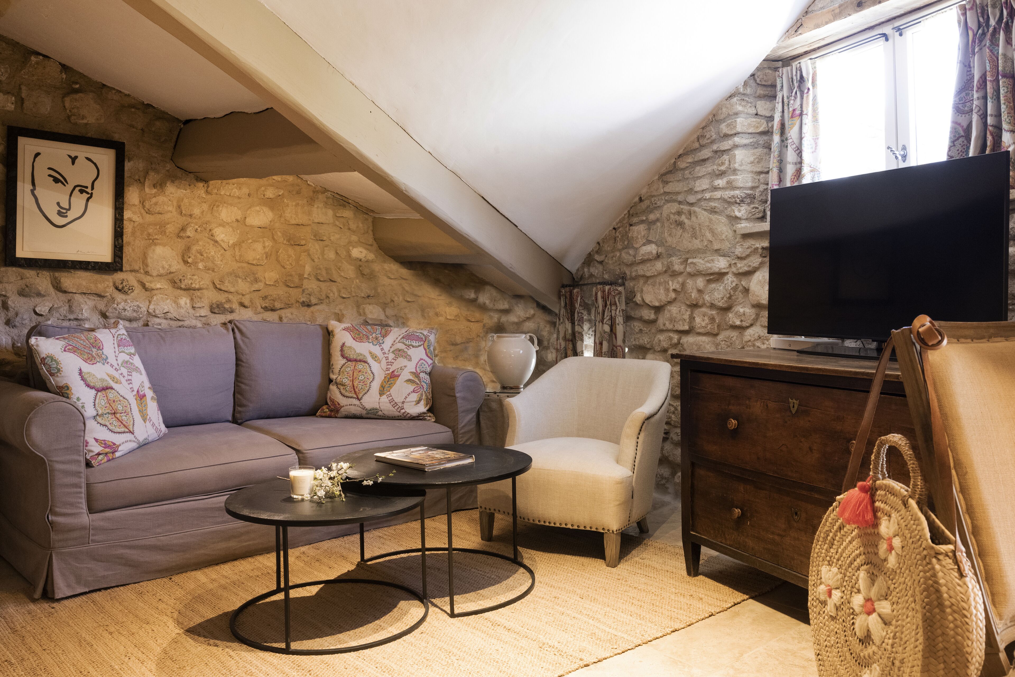 A cozy living room with a stone wall, a sofa, a chair, a coffee table, a TV, and a wooden cabinet.
