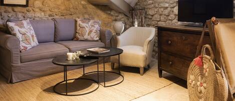 A cozy living room with a stone wall, a sofa, a chair, a coffee table, a TV, and a wooden cabinet.