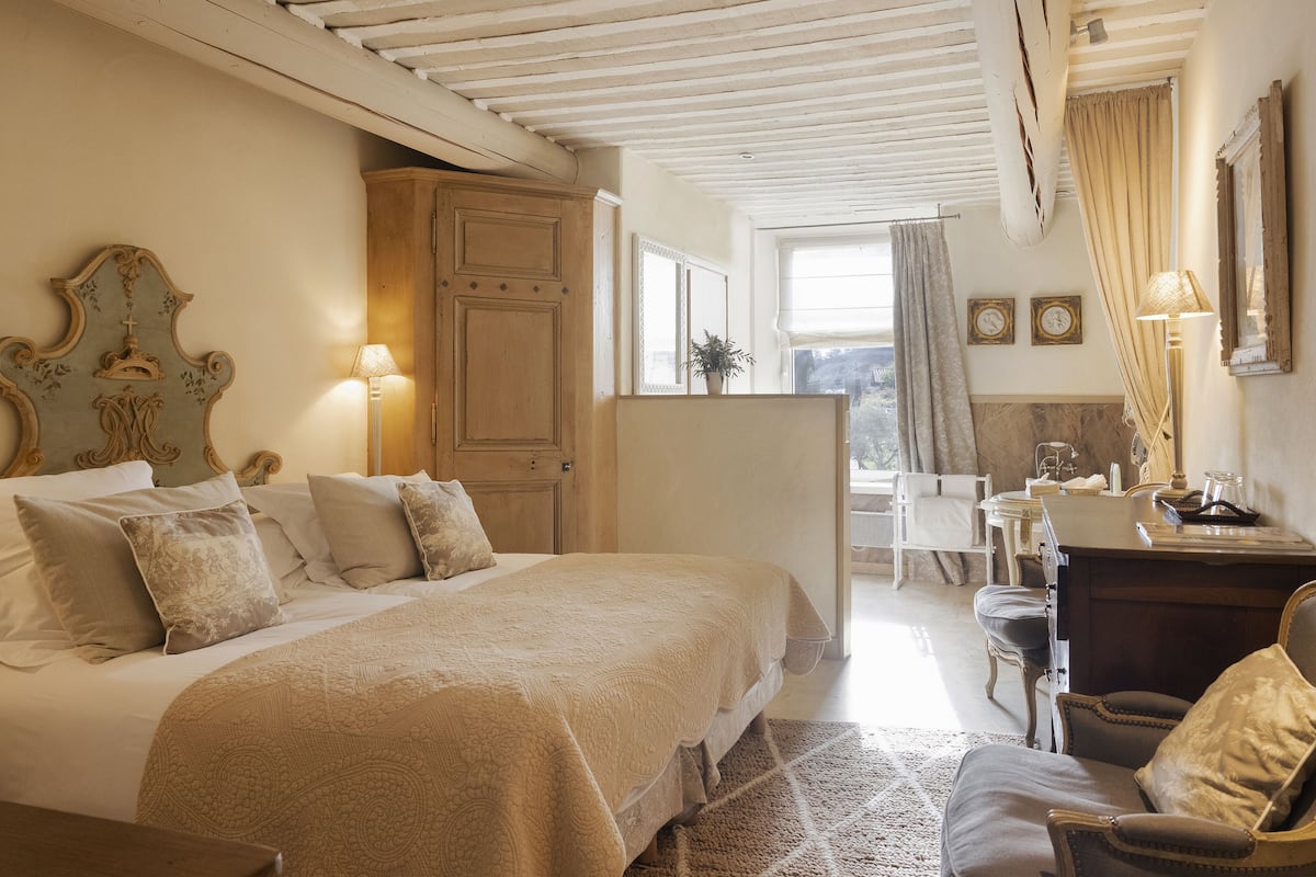 Une chambre avec un grand lit, une armoire en bois, un bureau avec une chaise et une vue sur l’extérieur.