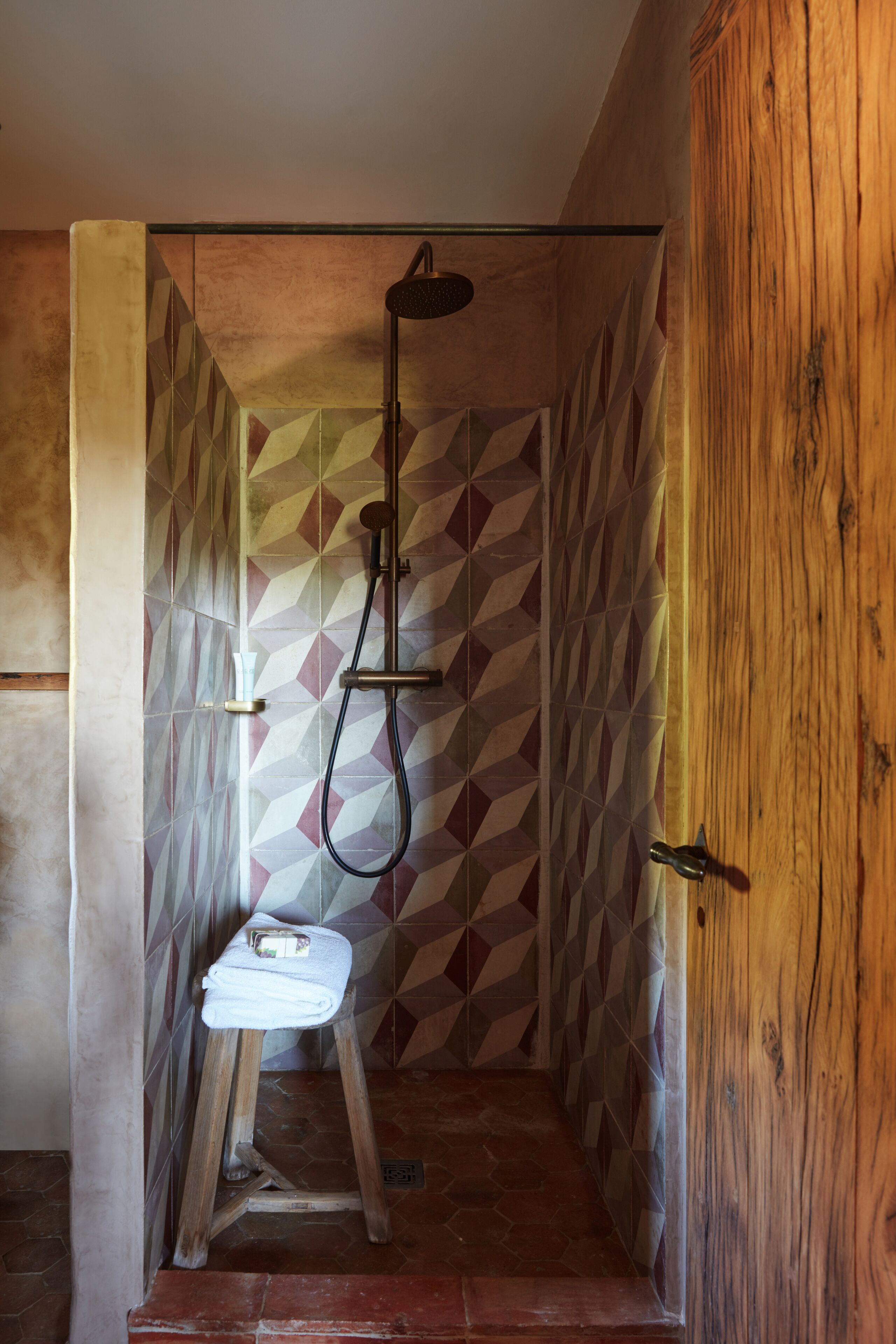 A shower area with a wooden door, a stool, and a geometric tile pattern on the walls.