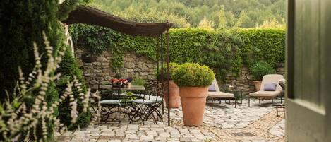 An outdoor patio with stone flooring, a table with chairs, a large potted plant, and a covered seating area.