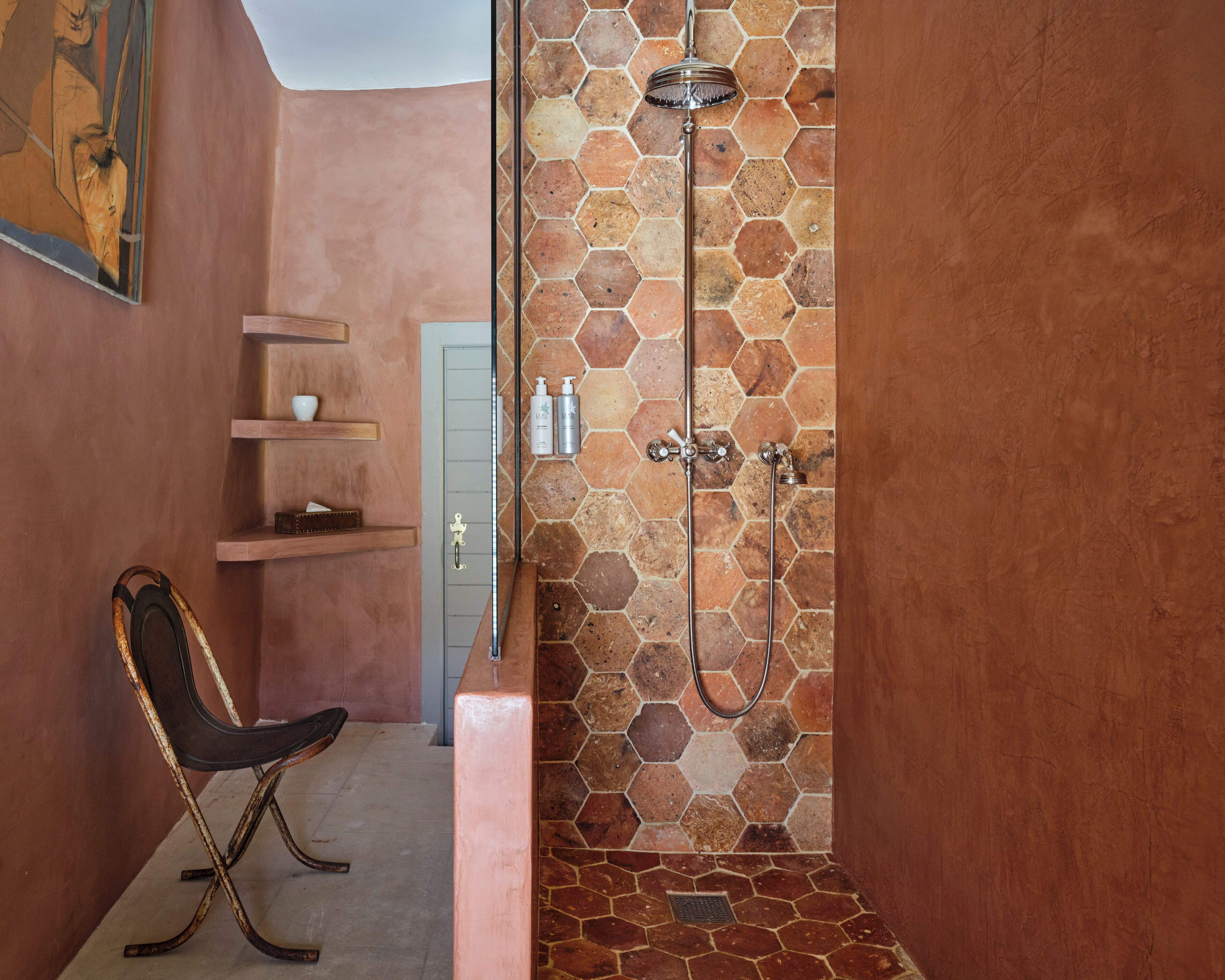 A bathroom with a shower, a chair, and a shelf with toiletries.