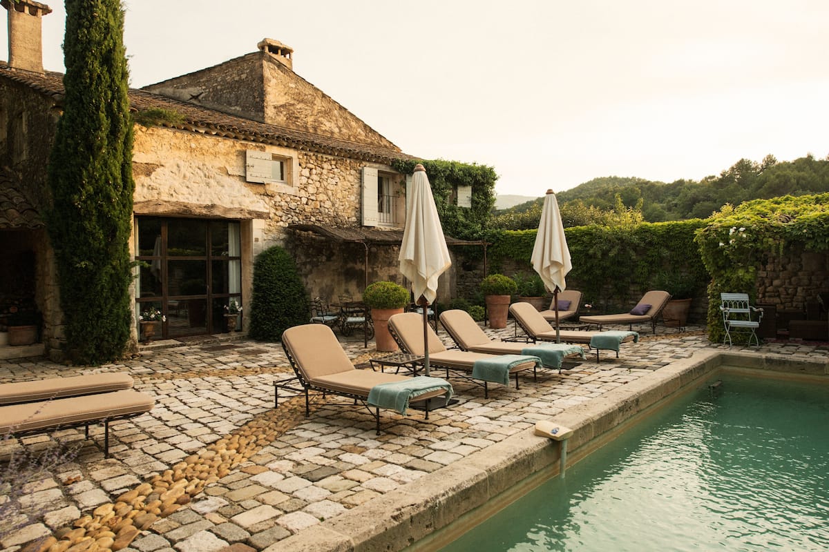 Un bâtiment en pierre doté d’une piscine, de chaises longues et de parasols.