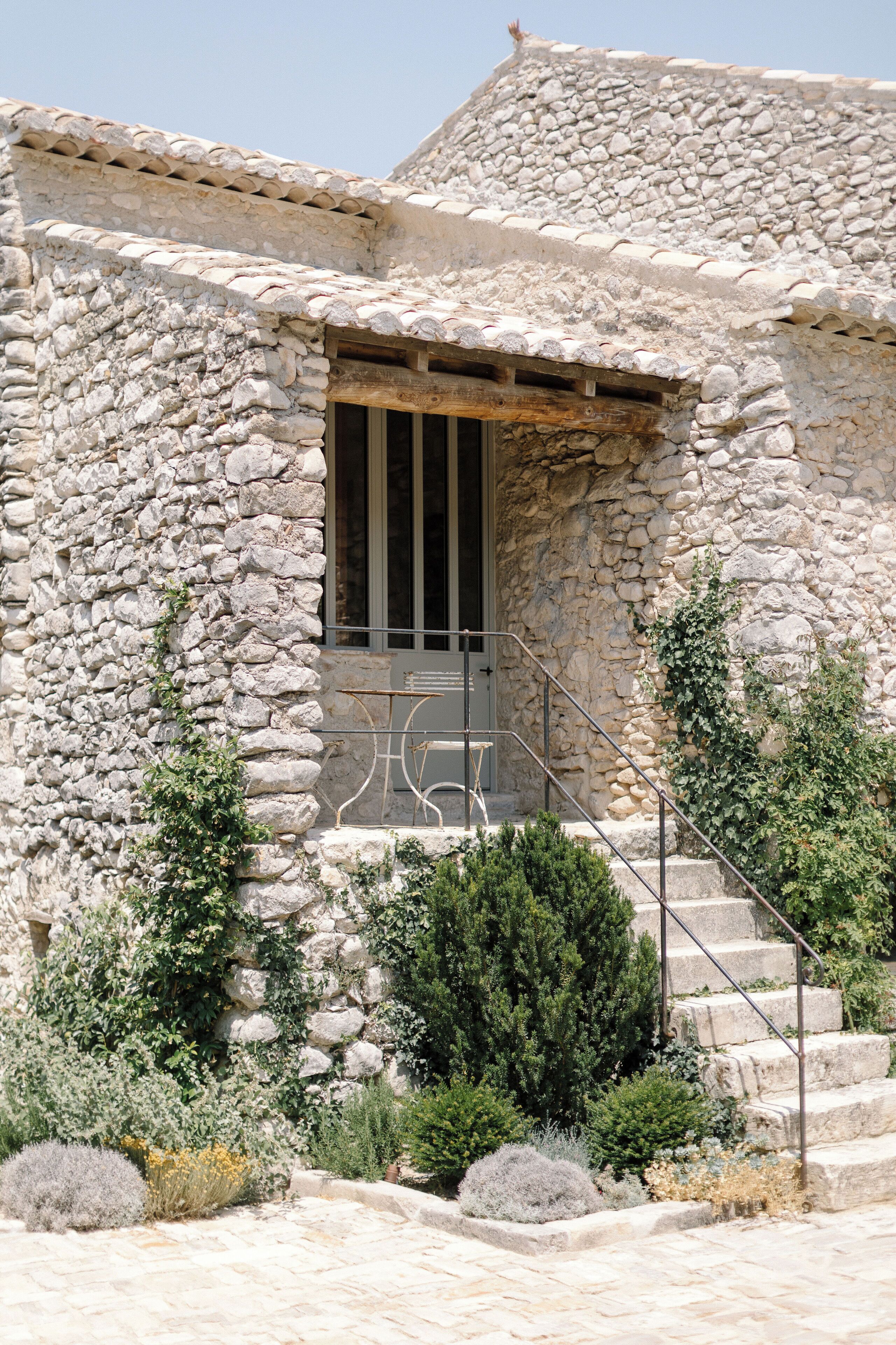 Un bâtiment en pierre avec une porte en bois et un escalier en métal menant à un petit espace de véranda.