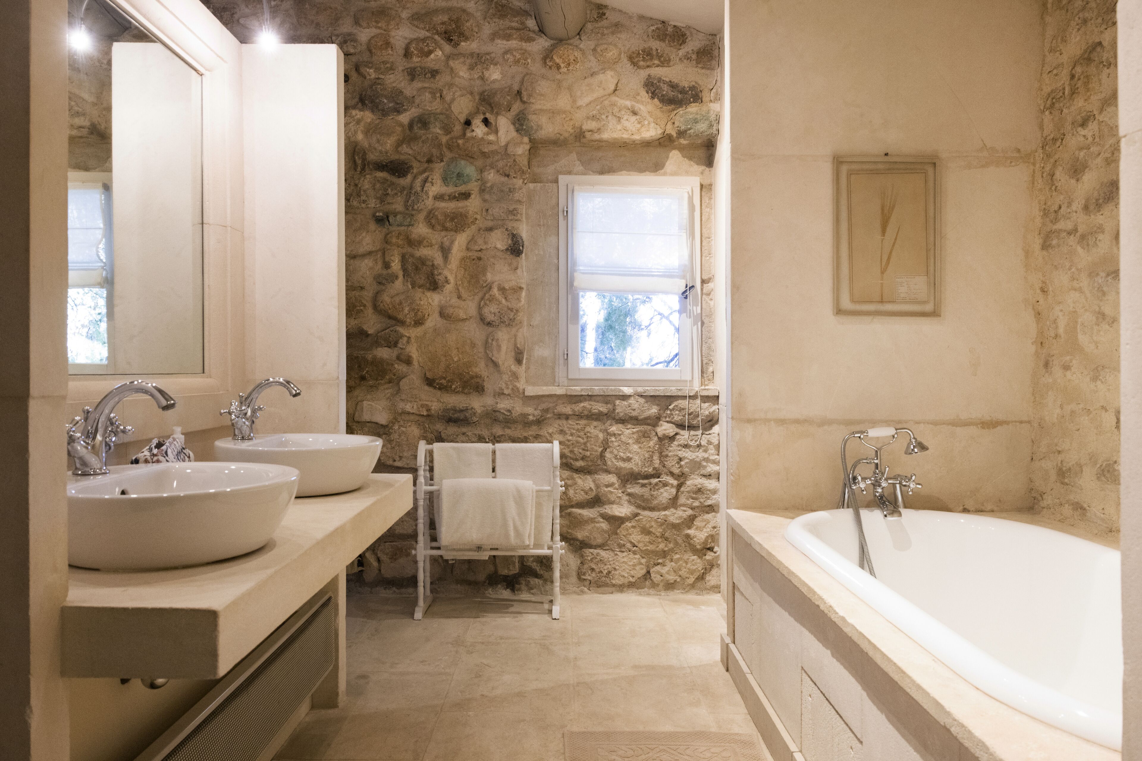 Un baño con dos lavamanos, una bañera, un perchero para toallas y una pared de piedra.