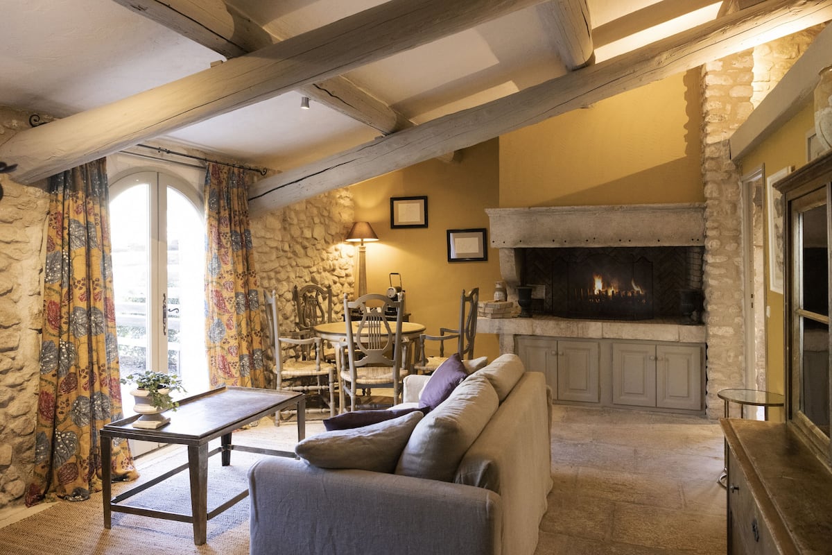 Un salon chaleureux avec une cheminée en pierre, des poutres apparentes et un canapé confortable.