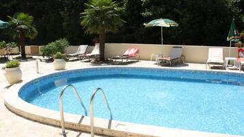 A swimming pool with lounge chairs and umbrellas, surrounded by potted plants and a tiled deck.