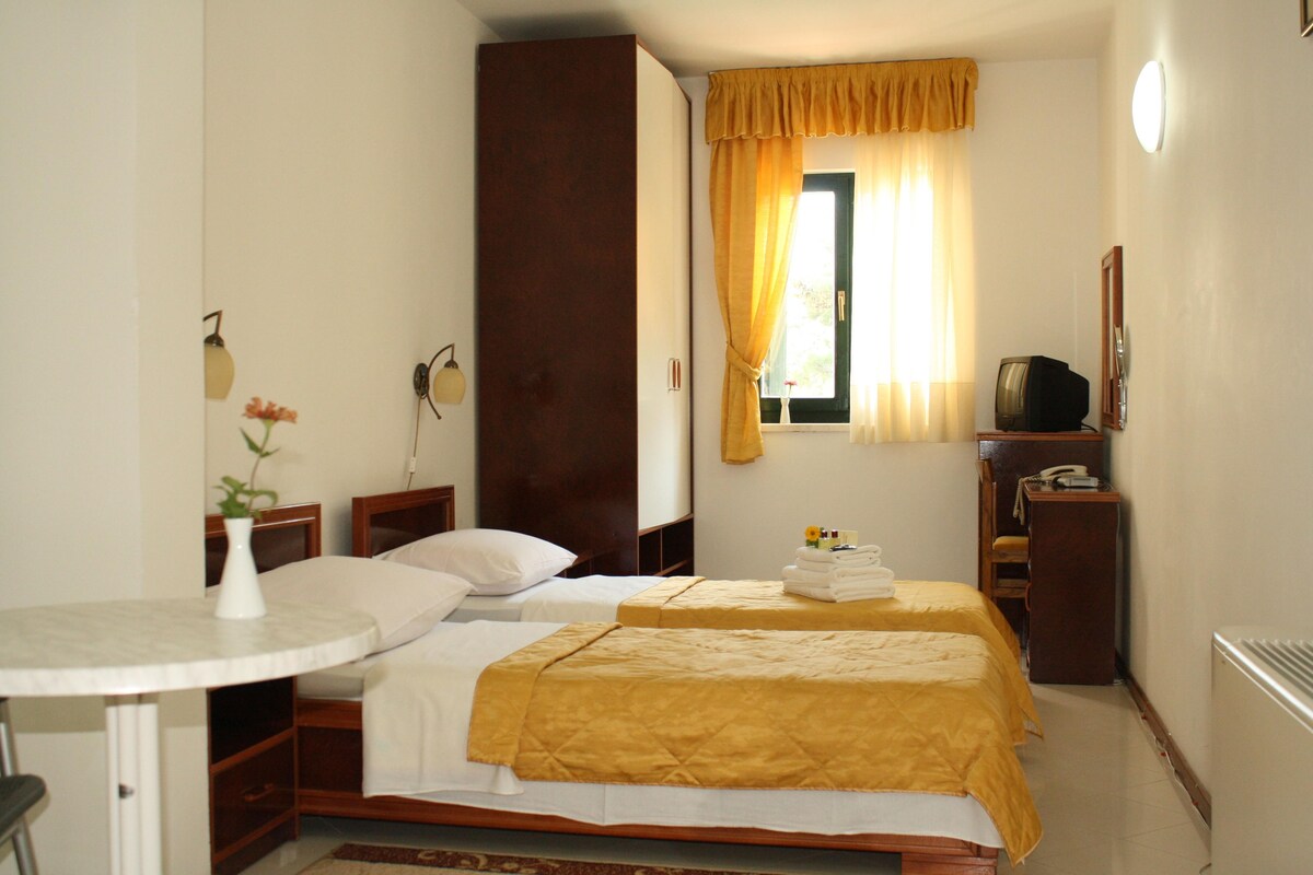 A hotel room with two beds, a small table, a TV, and a window with curtains.