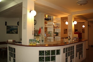 A bar area with shelves of bottles and glasses, a reception desk, and a window with a view.