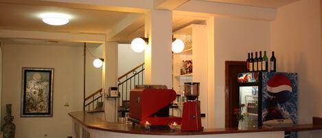 A kitchen area with a red coffee machine, a refrigerator with bottles, and a painting on the wall.