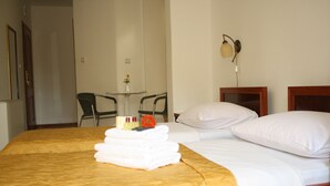 Una habitación de hotel con una cama, una mesita con sillas, una lámpara y un jarrón con una flor.