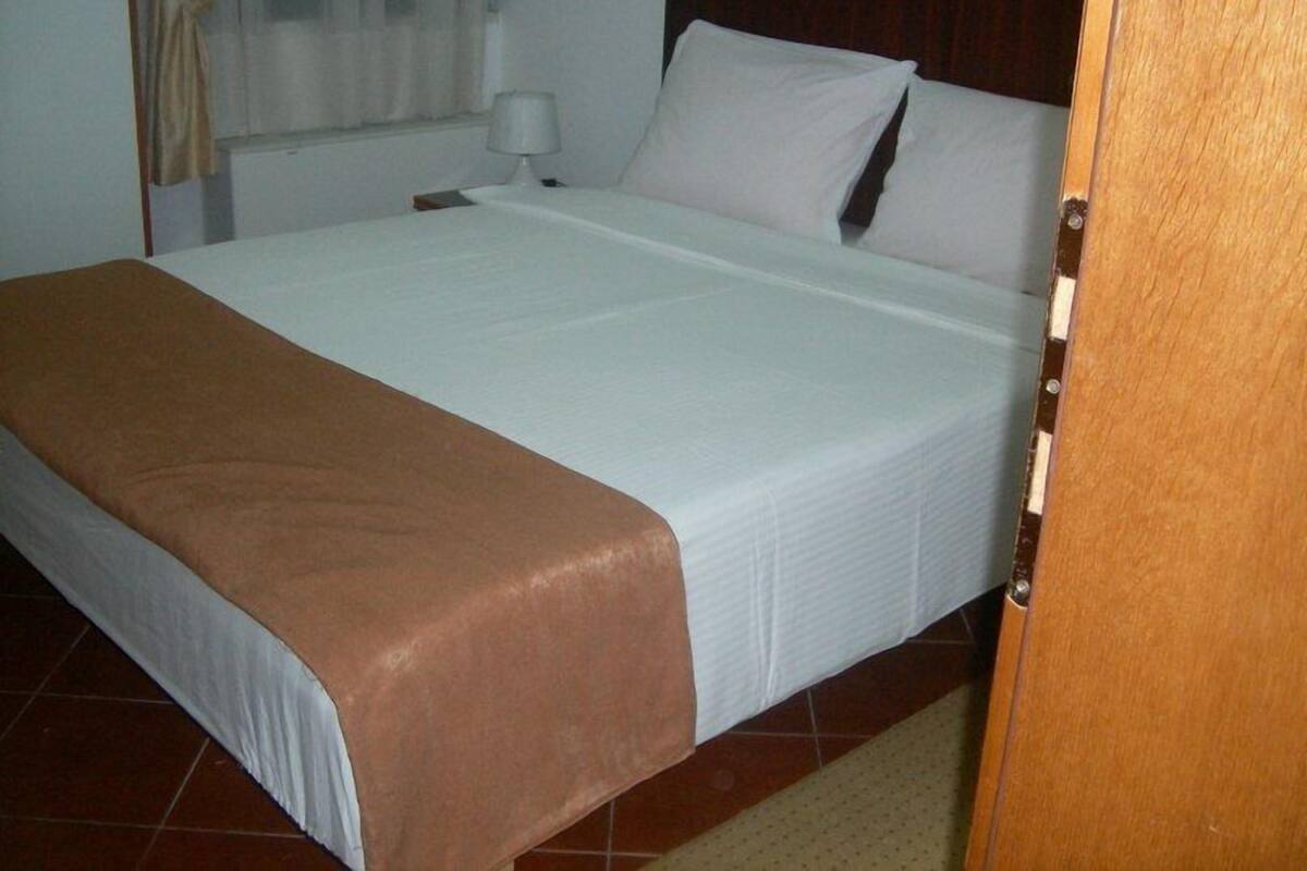A neatly made bed with a white and brown bedspread, a wooden headboard, and a nightstand with a lamp.