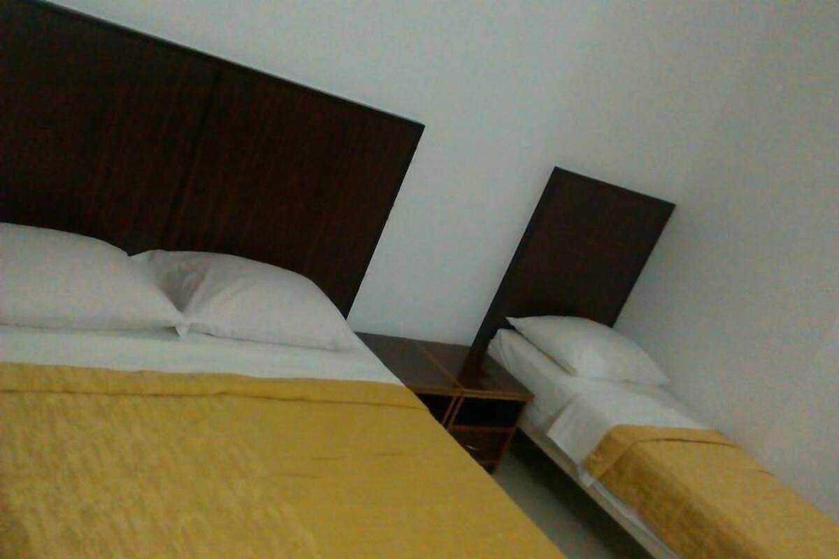 A hotel room with two single beds, each with a wooden headboard, white bedding, and a yellow blanket on one bed.
