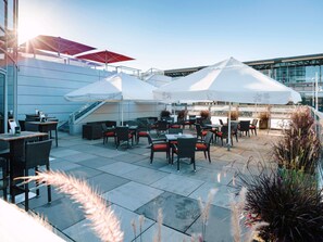 An outdoor seating area with tables and chairs, umbrellas, and a staircase leading to an upper level.