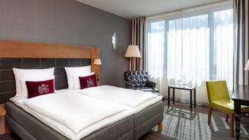 Een hotelkamer met een groot bed, een stoel, een klein tafeltje en een lamp.