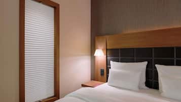 Een hotelkamer met een groot bed, een nachtkastje met een lamp en een raam met zonwering.
