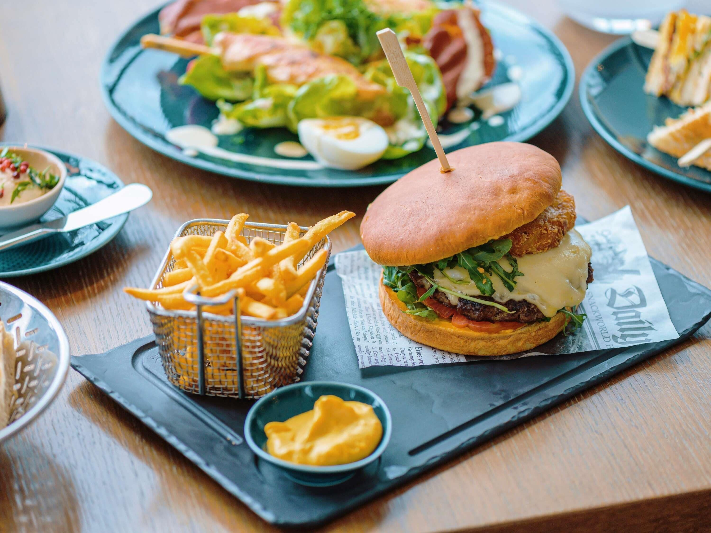 Comida con hamburguesa, papas fritas y ensalada sobre una mesa de madera.