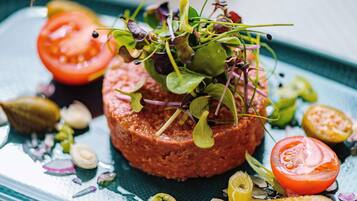 A dish with a central meat patty, garnished with greens and surrounded by sliced tomatoes and pickles.
