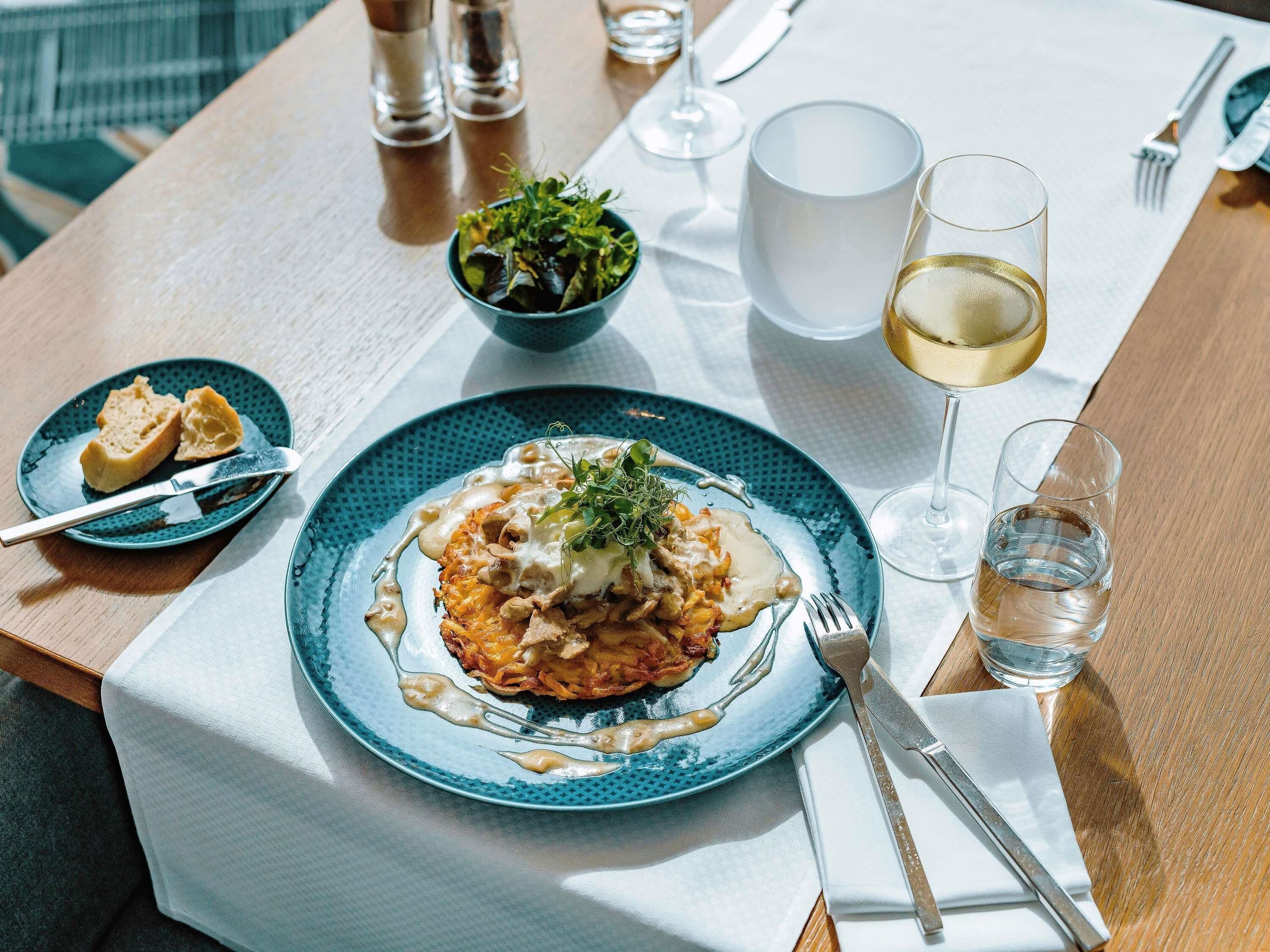 A table with a plate of food, a glass of white wine, and a bowl of salad.