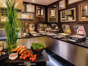 Zona de buffet con diversos alimentos, una planta y espejos decorativos en la pared.