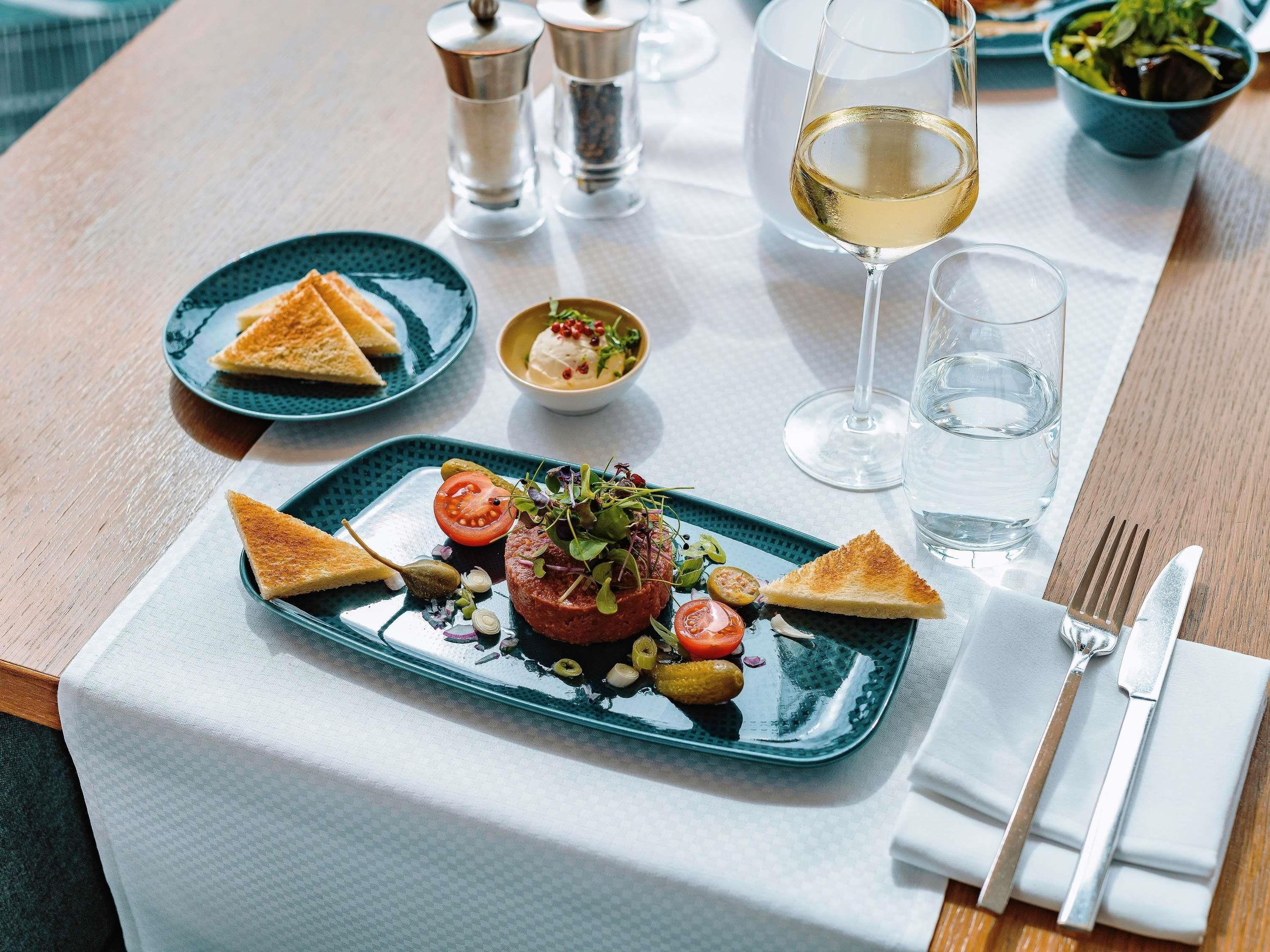 Una mesa de comedor con un plato de comida, una copa de vino blanco y un bol de ensalada.