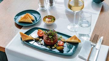Una mesa de comedor con un plato de comida, una copa de vino blanco y un bol de ensalada.