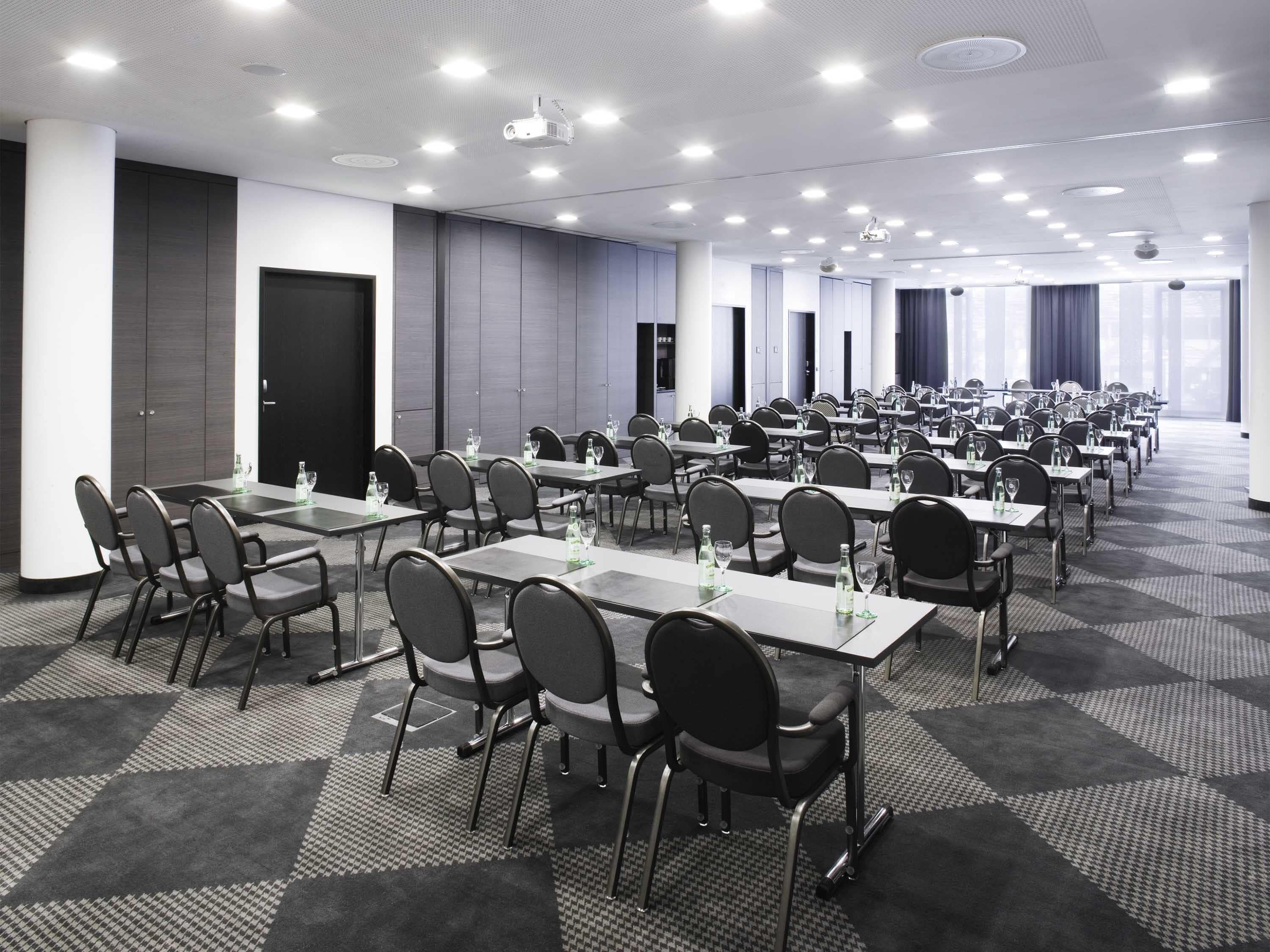 A conference room with multiple tables and chairs, equipped with projectors and ceiling lights.