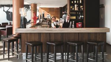 Zona de bar con mostrador de madera, taburetes y una estantería para vinos con botellas.