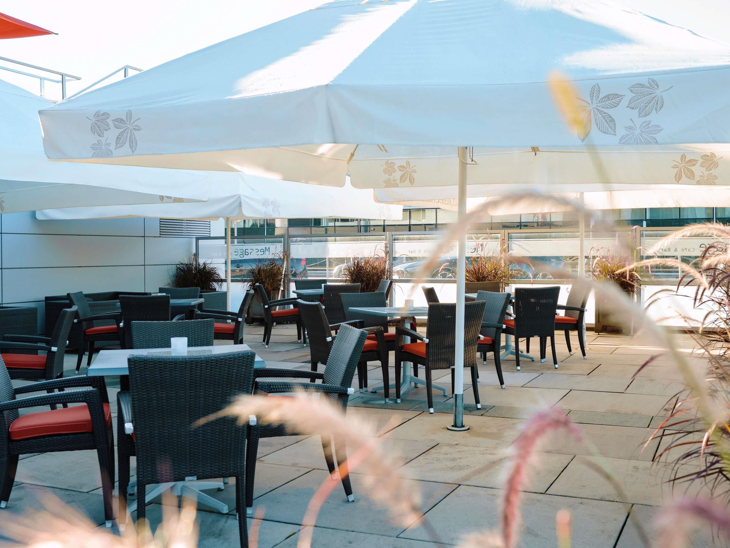 An outdoor seating area with wicker chairs and tables, covered by large umbrellas, and potted plants.