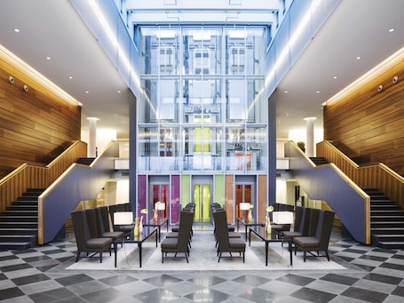 A modern lobby with a central staircase, glass walls, and a checkered floor.. Mövenpick Hotel Stuttgart Airport