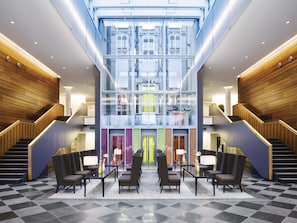 A modern lobby with a central staircase, glass walls, and a checkered floor.