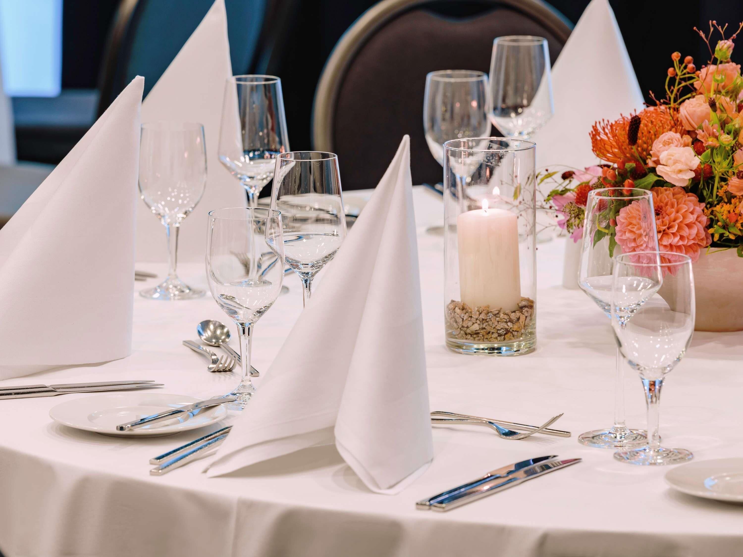Une table dressée avec de la vaisselle transparente, des serviettes blanches et un chandelier en guise de décoration centrale.