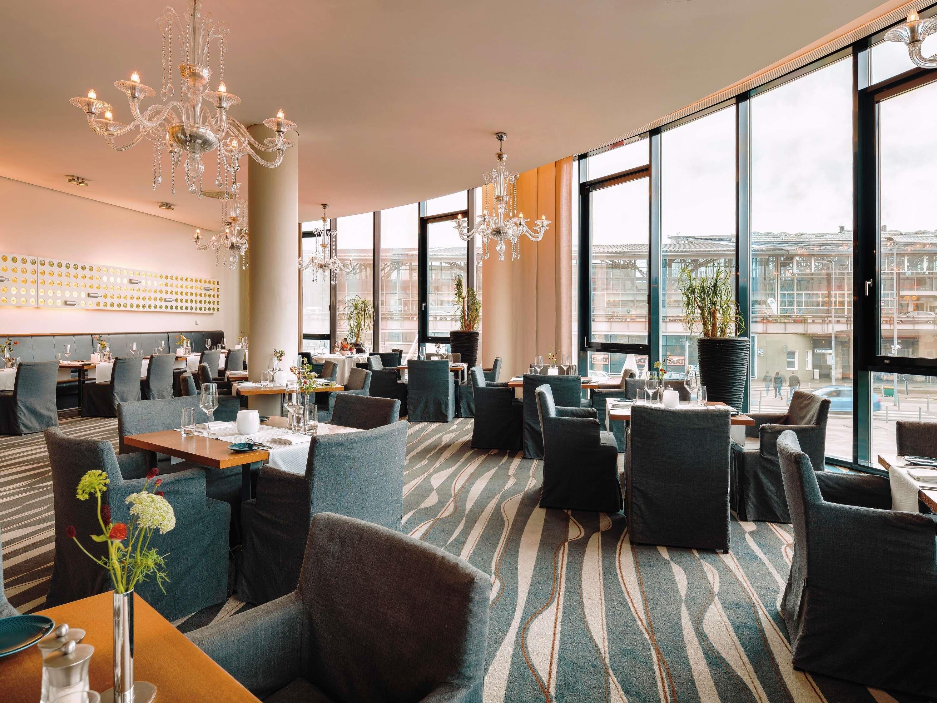 A modern restaurant with high ceilings, large windows, and a patterned carpet.
