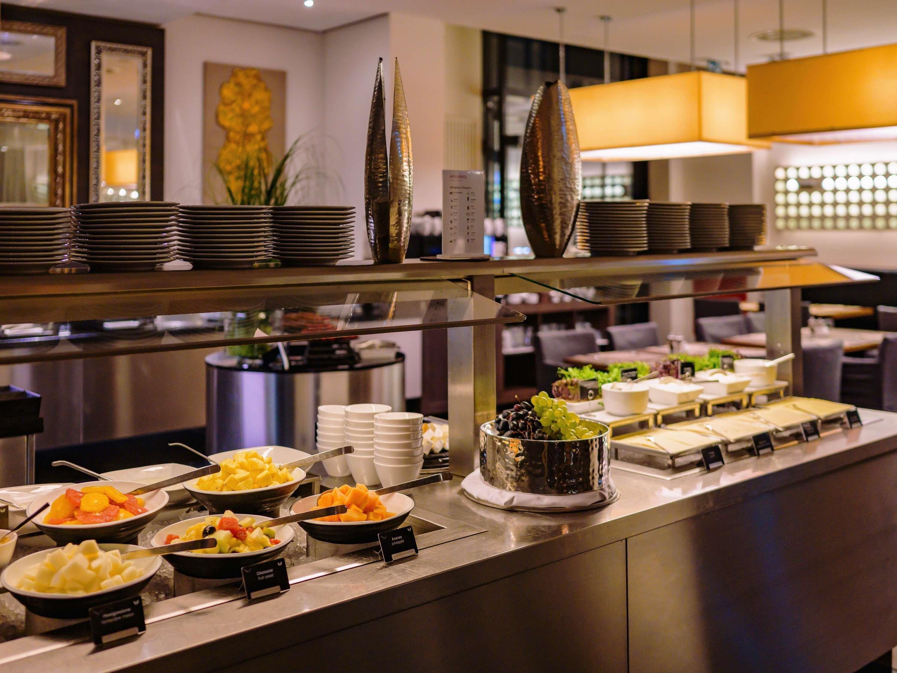 En buffé med ett varierat utbud av mat, inklusive frukt och ost, i en modern hotellmiljö.