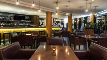 A restaurant with wooden tables and chairs, a bar area with bottles, and a mural on the wall.
