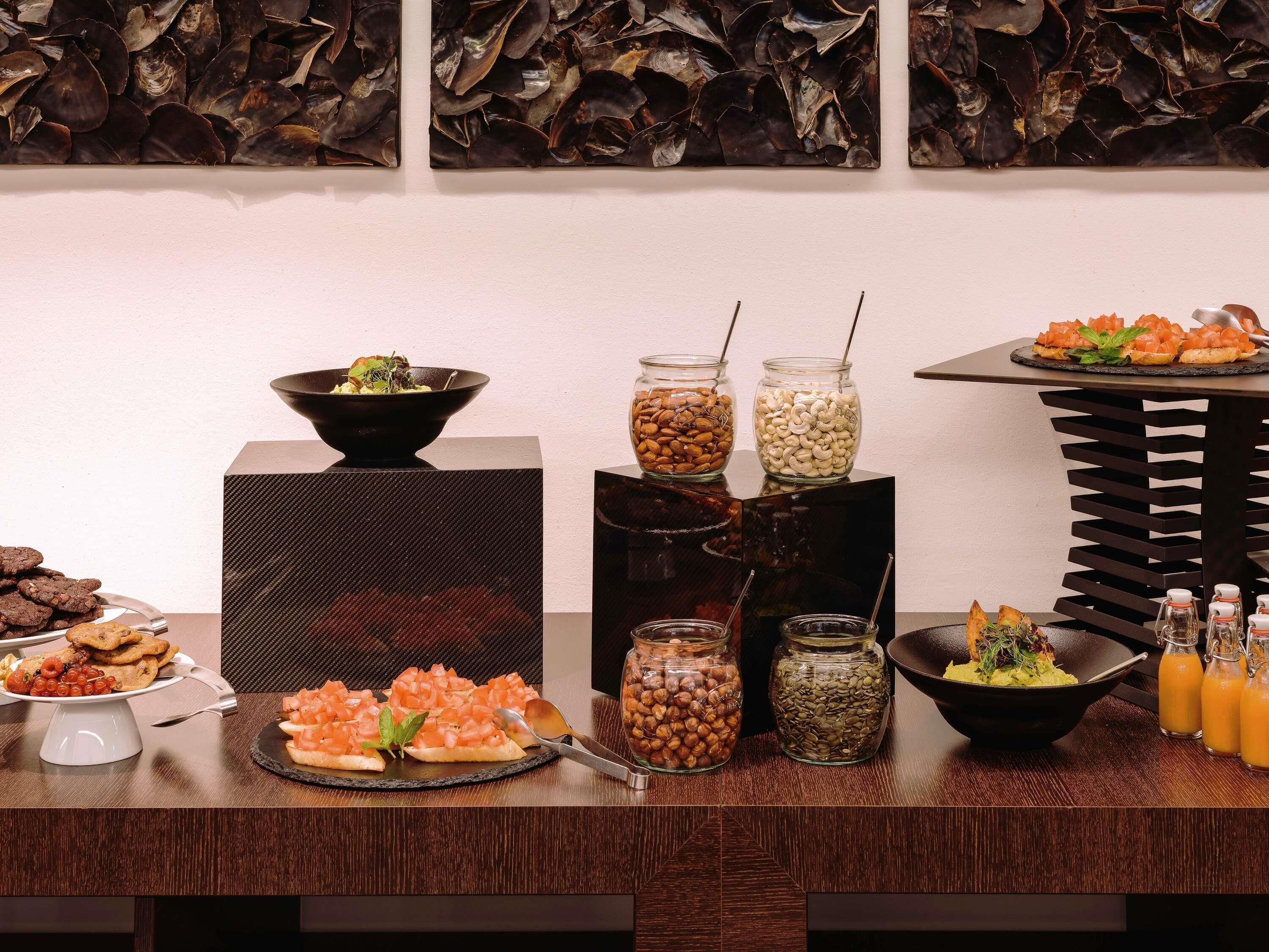 Una mesa de buffet con diversos alimentos, como un tazón de ensalada, frascos con frutos secos y un plato de aperitivos.