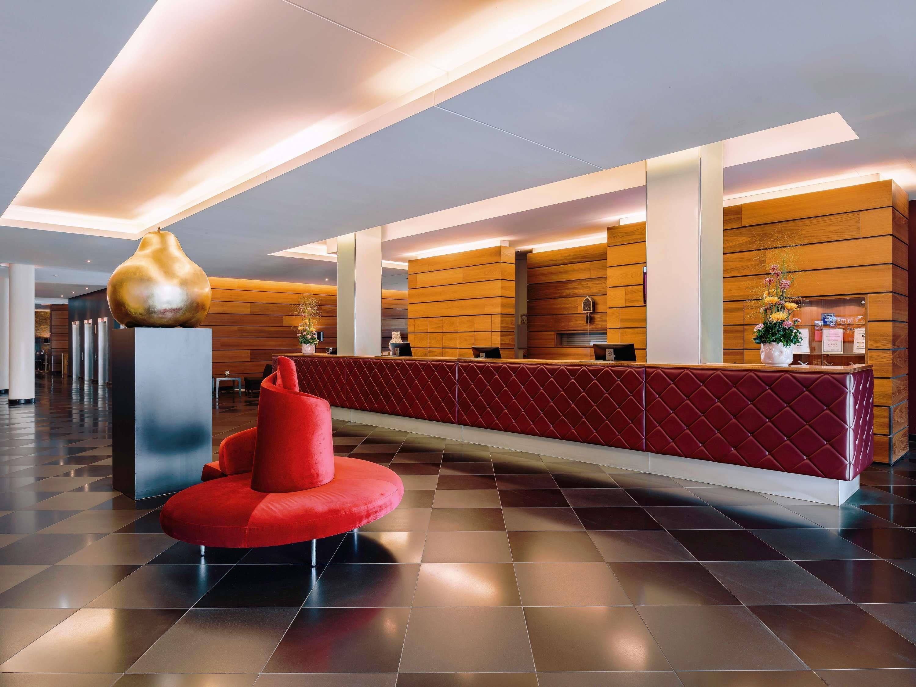 A modern reception area with a red cushioned bench, a large gold sculpture, and wooden paneling.