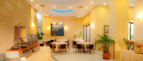 A hotel dining area with buffet service, tables, chairs, and a large painting on the wall.