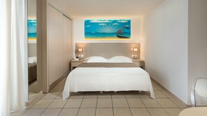 Ein Hotelzimmer mit Bett, Nachttisch, einem an der Wand hängenden Gemälde eines Segelbootes und Blick durch eine Schiebetür.