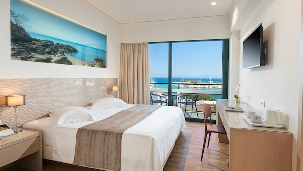 Ein Hotelzimmer mit Bett, Schreibtisch, Stuhl, Fernseher und einem großen Fenster mit Meerblick.