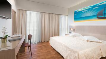 A hotel room with a bed, a desk, a chair, a TV, and a painting of a sailboat on the wall.