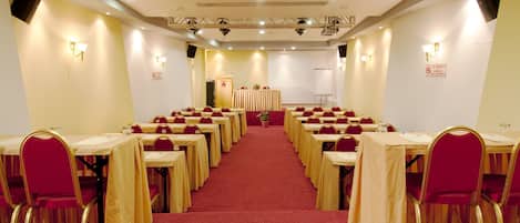 Un salón de conferencias con filas de mesas y sillas, un atril y suelo alfombrado.