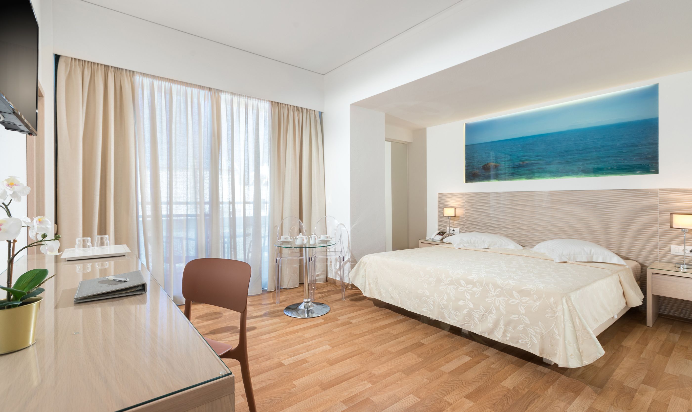 Habitación de hotel con cama, escritorio, silla, una mesita y un cuadro marino en la pared.