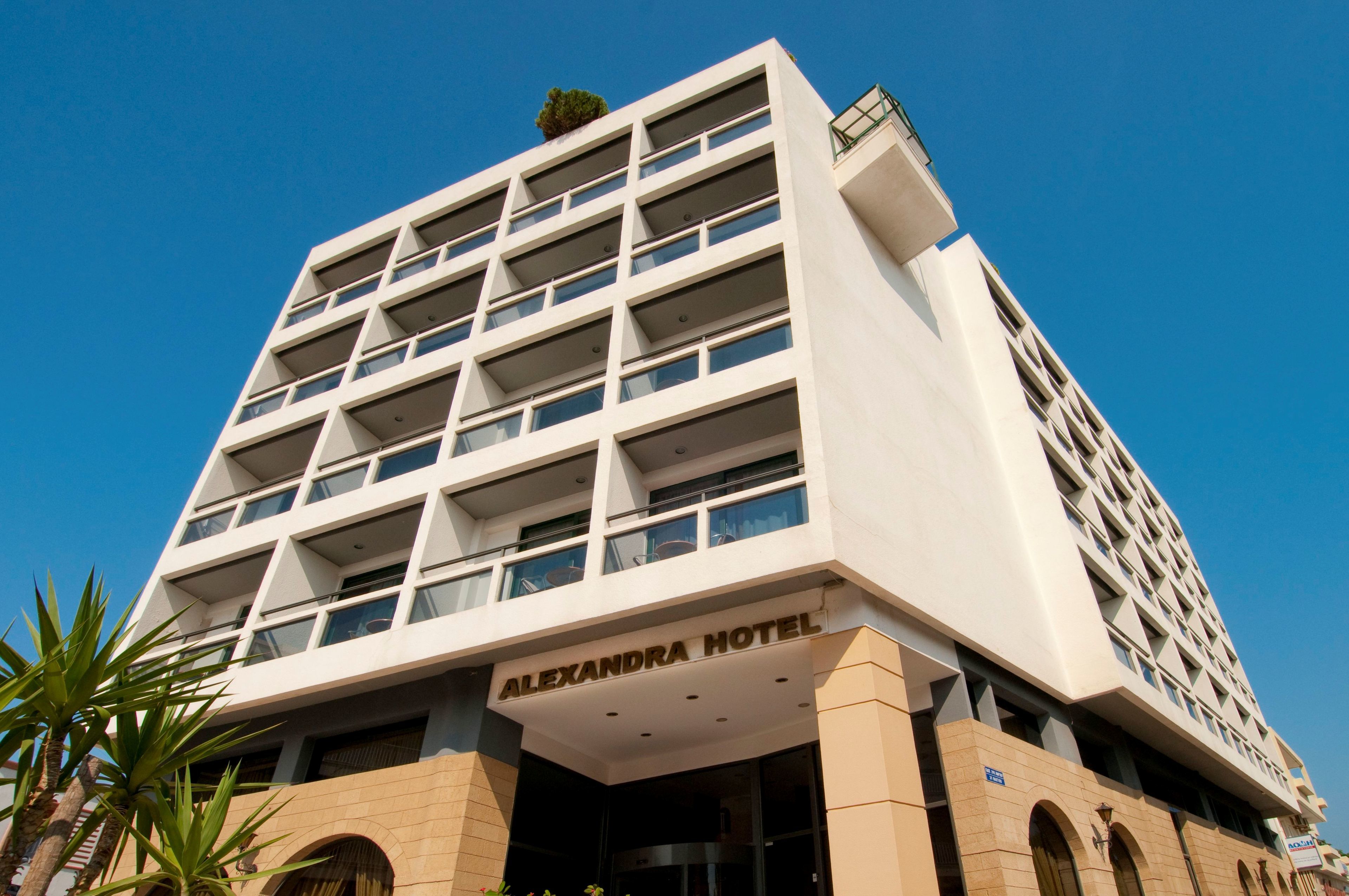 Un hôtel moderne, reconnaissable à son enseigne bien visible où l’on peut lire « HÔTEL ALEXANDRA ».