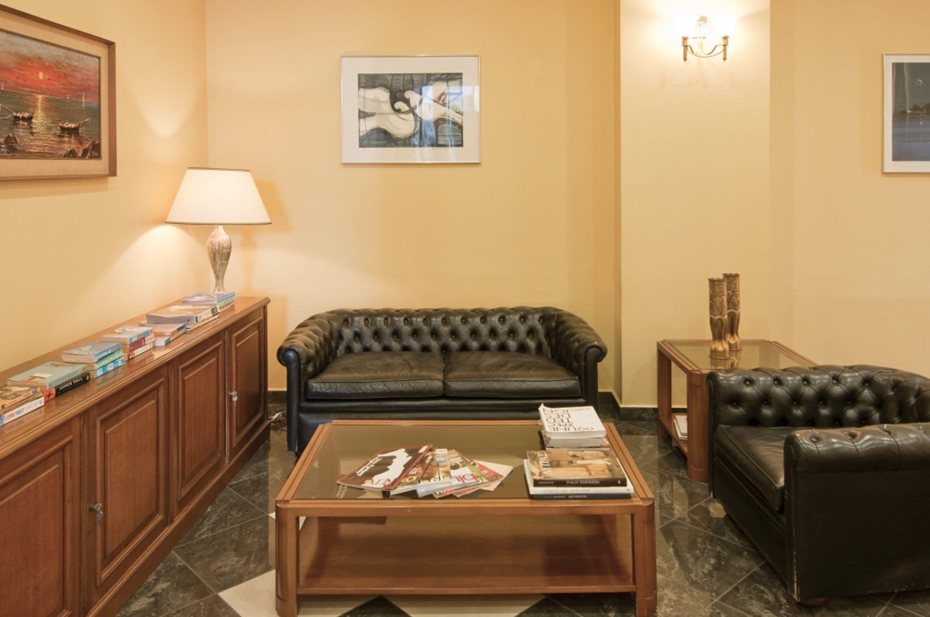 Una sala de estar con un sofá de cuero, una mesa de centro con revistas, una lámpara y una estantería.