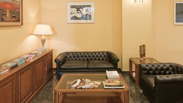 Una sala de estar con un sofá de cuero, una mesa de centro con revistas, una lámpara y una estantería.