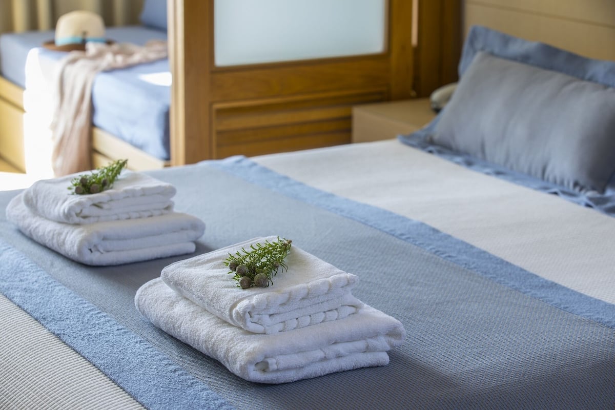 A neatly made bed with white towels and a small plant, a wooden headboard, and a blue pillow.